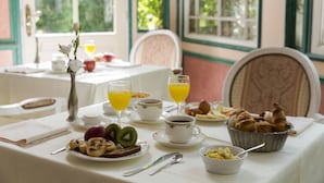 A breakfast table with various food items, cups of coffee and juice, and a vase with flowers.