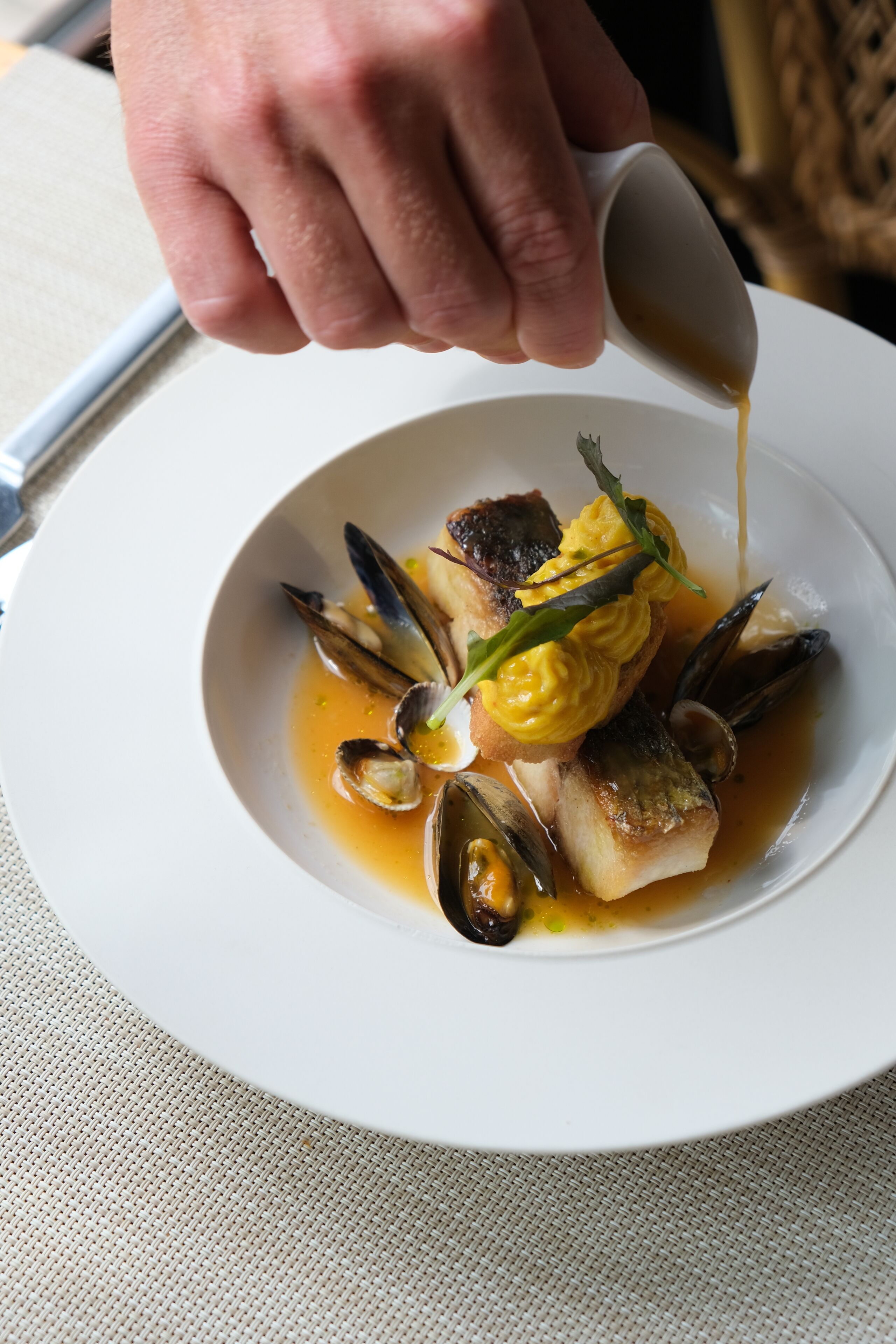 Un plato blanco con mejillones, pescado y salsa que se vierte sobre ellos.