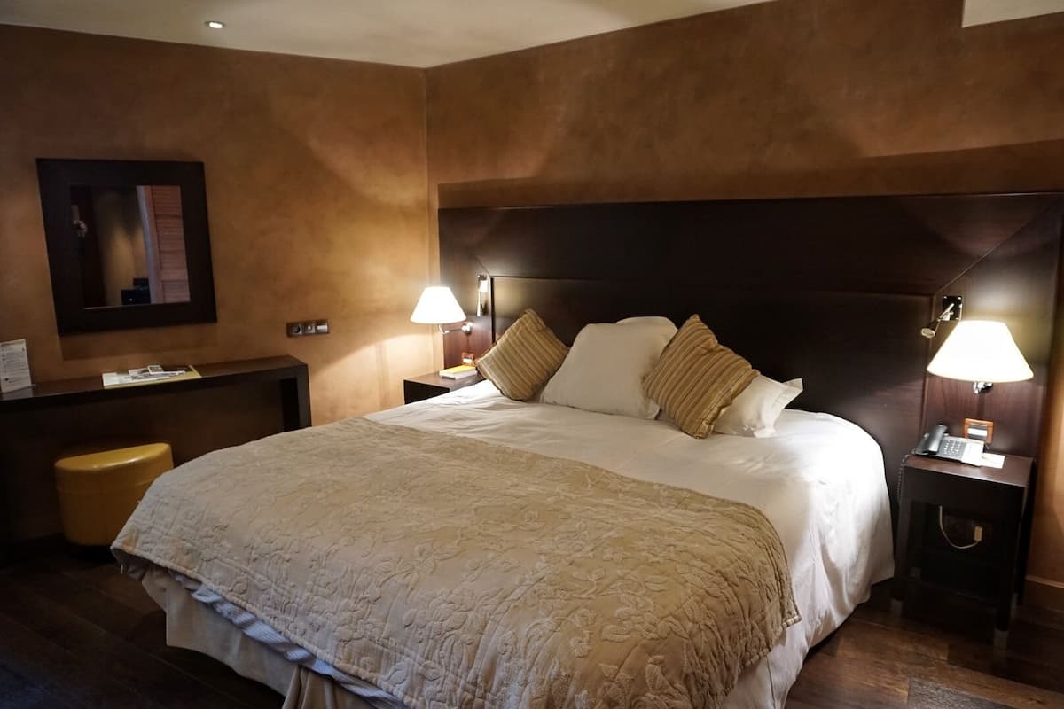 Habitación de hotel con una cama grande, dos mesitas de noche con lámparas, un escritorio y una silla.