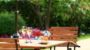 Une terrasse extérieure avec une table et des chaises en bois, une lampe en métal et un verre de jus d’orange.