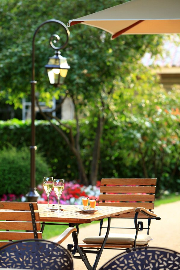 Un patio exterior con una mesa y sillas de madera, una lámpara de metal y un vaso de jugo de naranja.