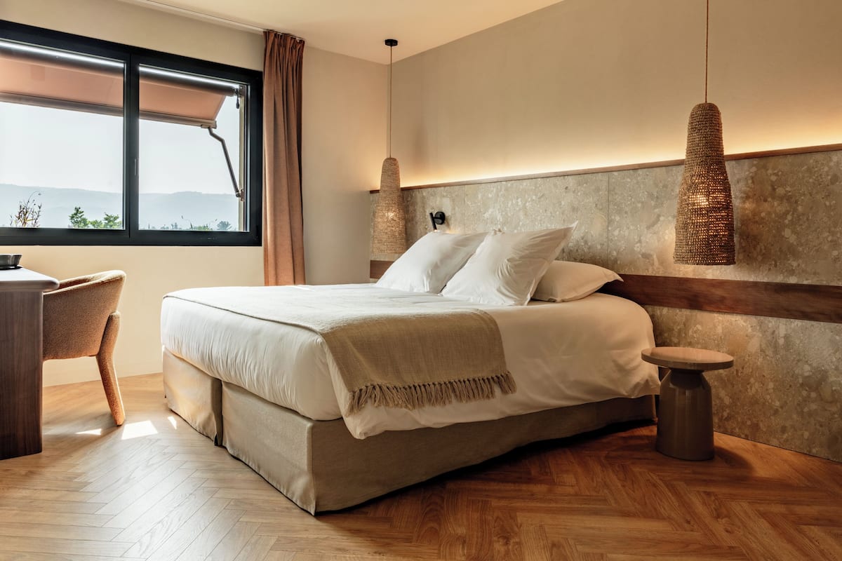 A bedroom with a bed, bedside tables, a desk, and a window with a view.