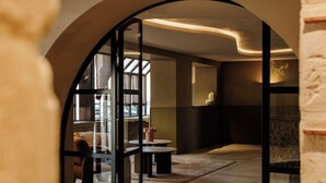 An interior with a curved archway, a seating area with a table and chairs, and a large window allowing natural light. - La Maison Chabran - Hôtel Restaurants (Pont-de-l'Isere)