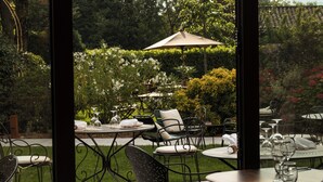 An outdoor patio with tables and chairs, surrounded by lush greenery and trees. - La Maison Chabran - Hôtel Restaurants (Pont-de-l'Isere)