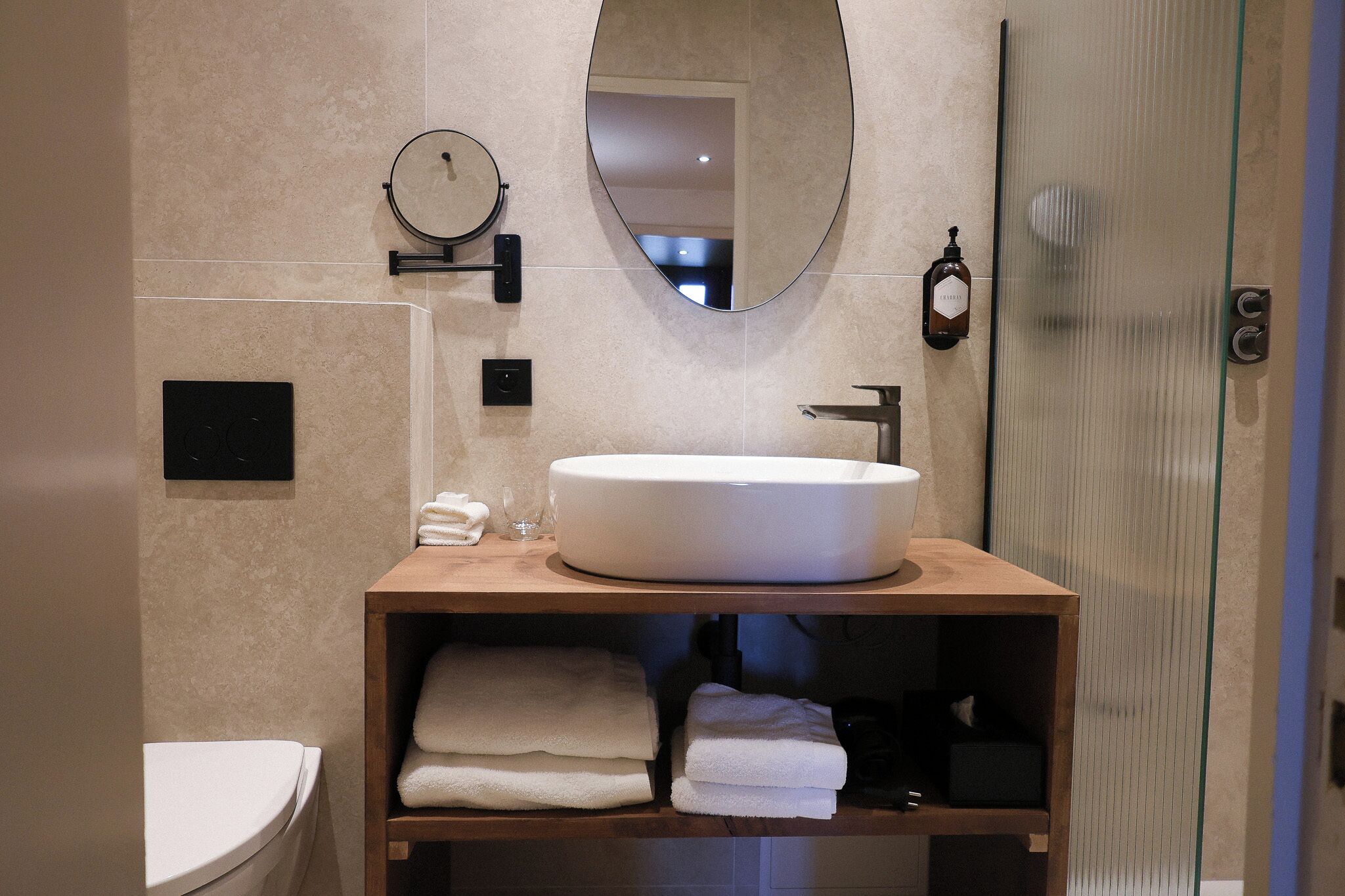 A modern bathroom with a round mirror, a large oval mirror, a white sink, and a glass shower enclosure.
