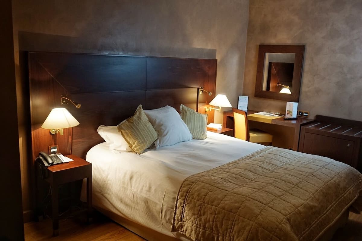 A hotel room with a large bed, bedside lamps, a desk with a phone, and a mirror on the wall.