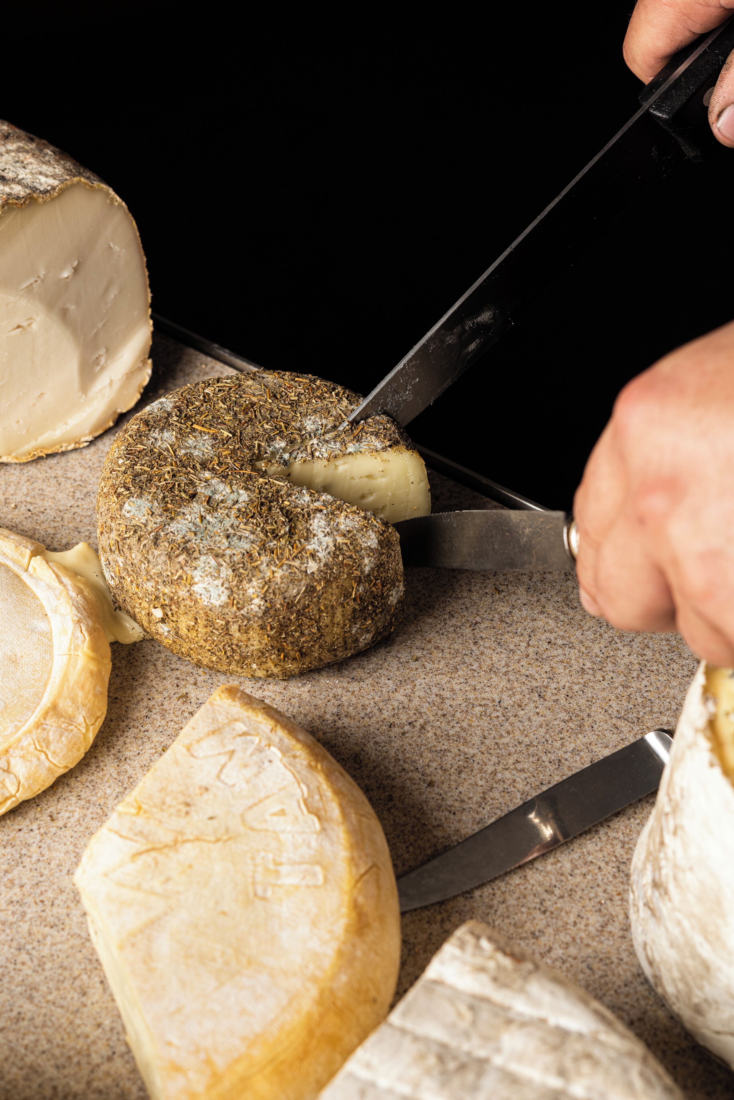 A variety of cheeses with a knife cutting through one.