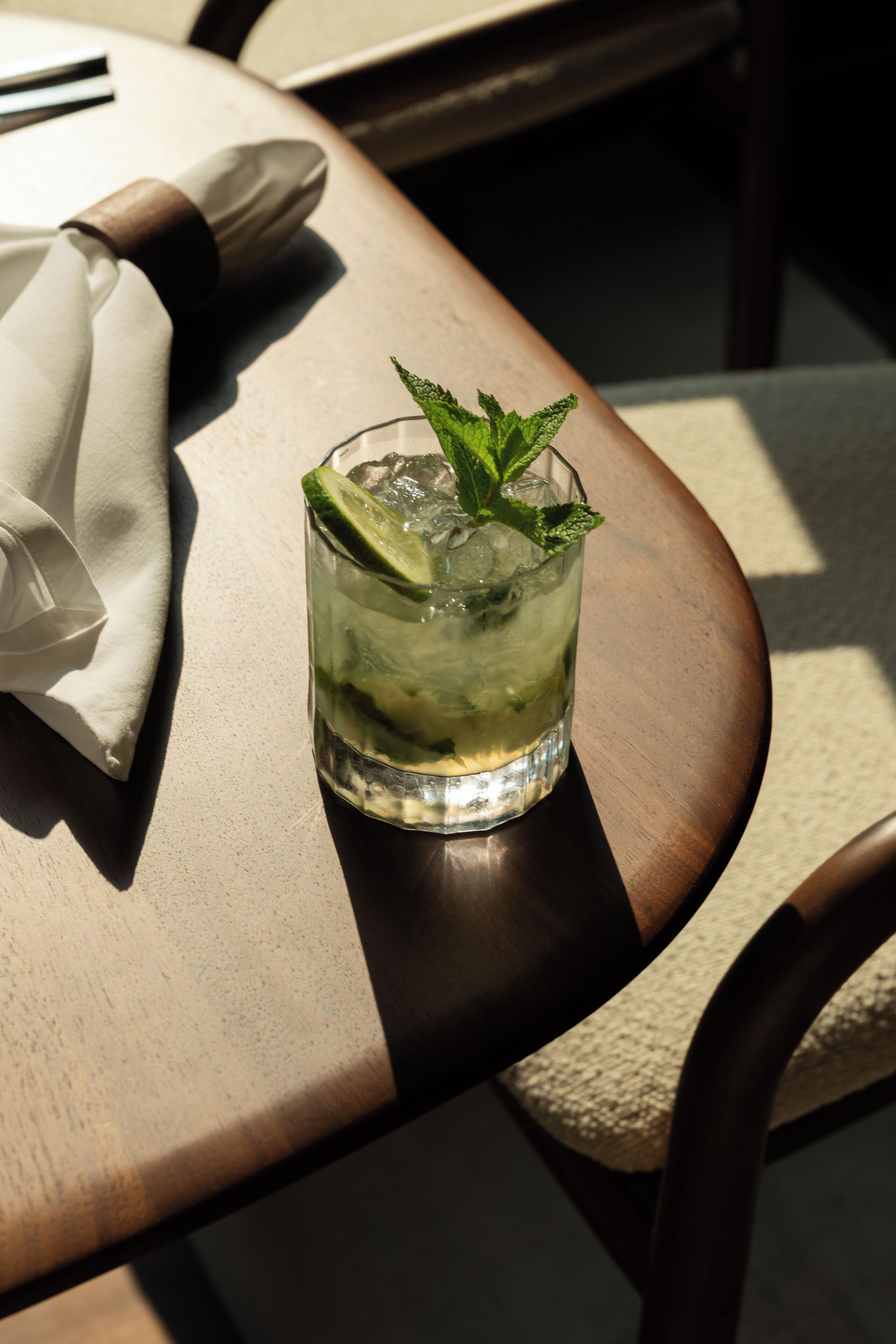 Un vaso de bebida con lima y menta sobre una mesa de madera.