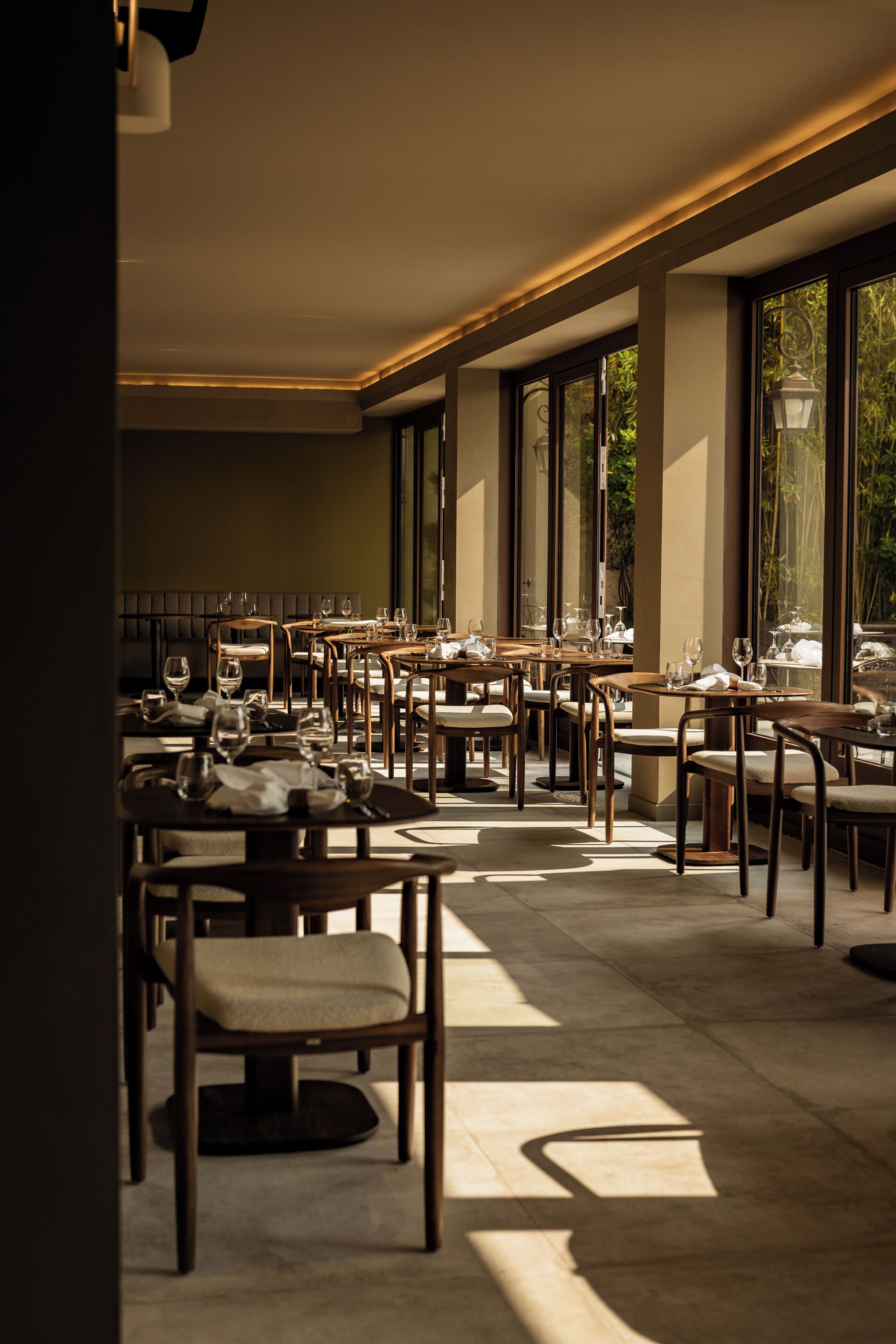 Un restaurant moderne doté de nombreuses tables et chaises, de grandes fenêtres et d’un intérieur épuré et minimaliste.