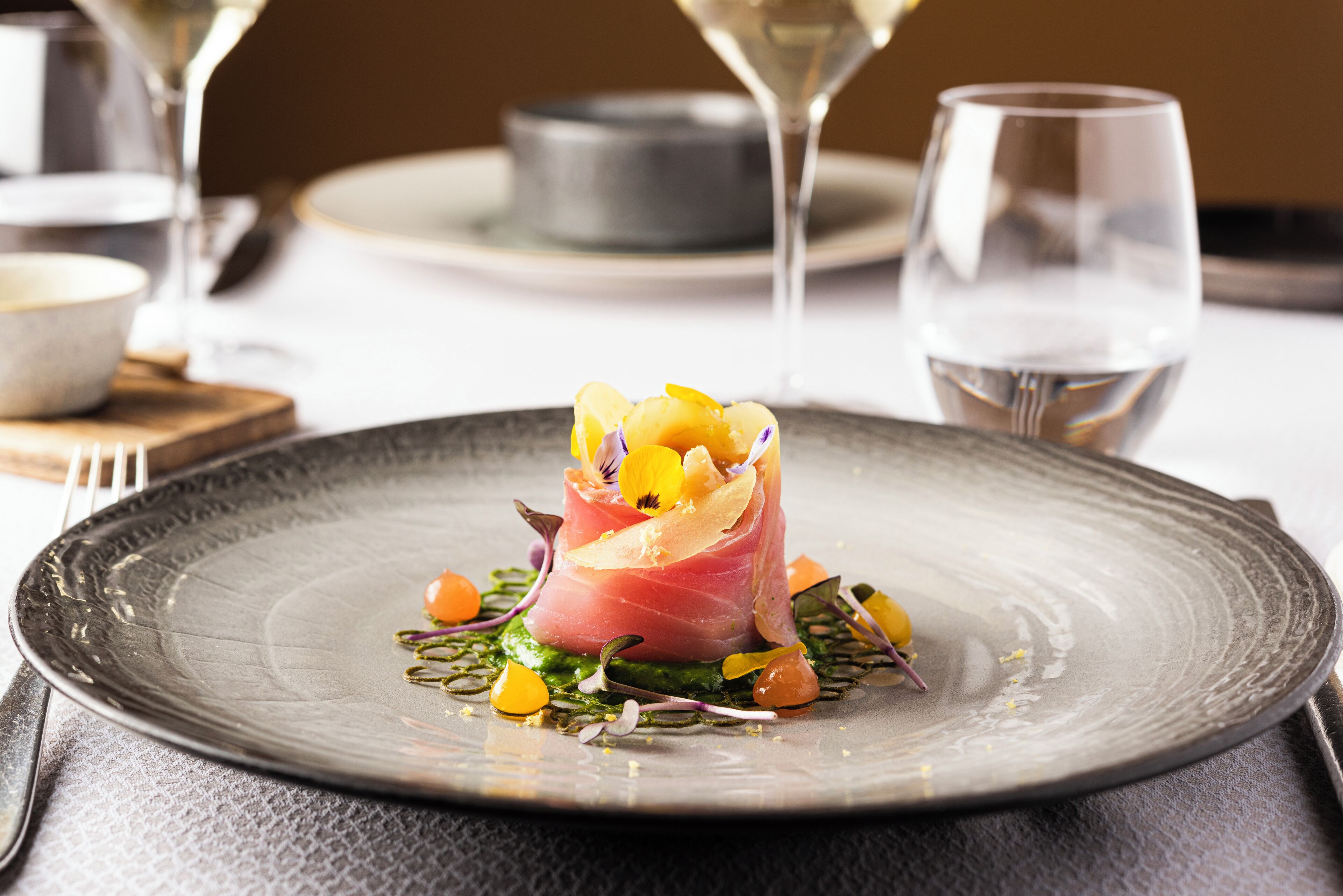 Une assiette avec une présentation soignée des plats, un verre de vin blanc et un bol en arrière-plan.