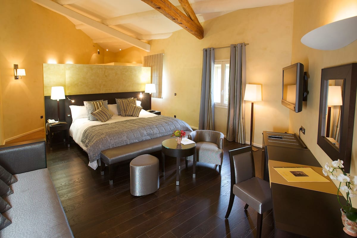 A hotel room with a bed, a desk, a chair, a sofa, and a small table.