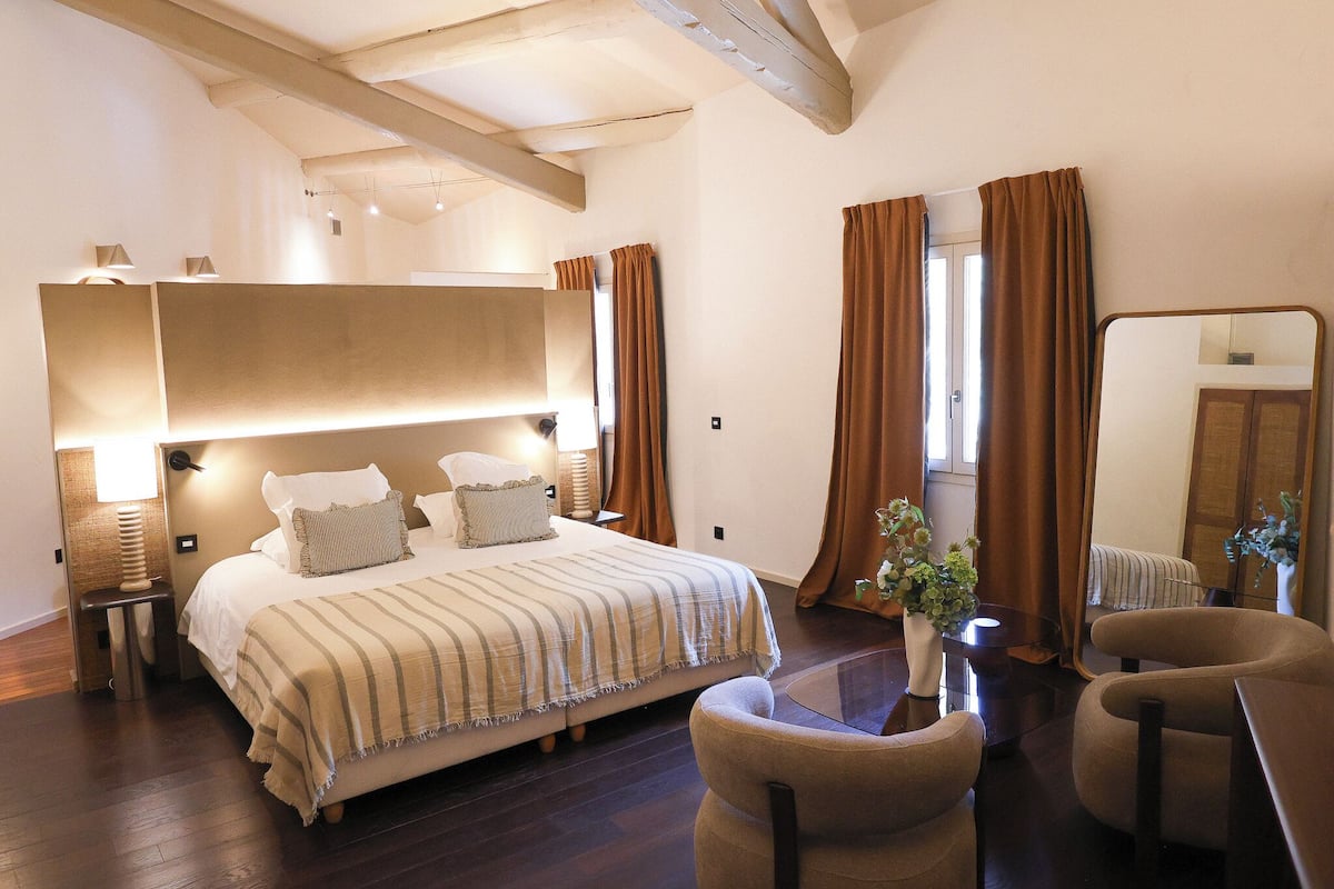 A hotel room with a large bed, bedside lamps, a small table with a vase, and a chair.