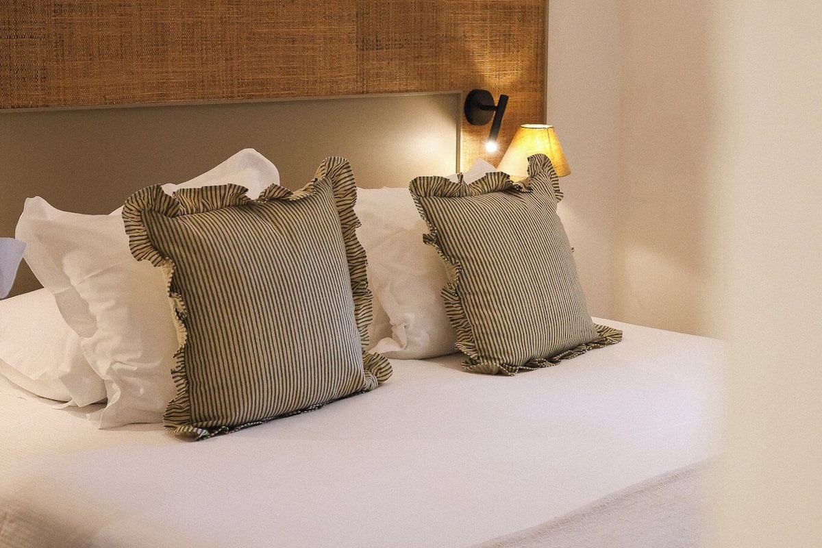 A neatly made bed with two pillows, a bedside lamp, and a headboard.