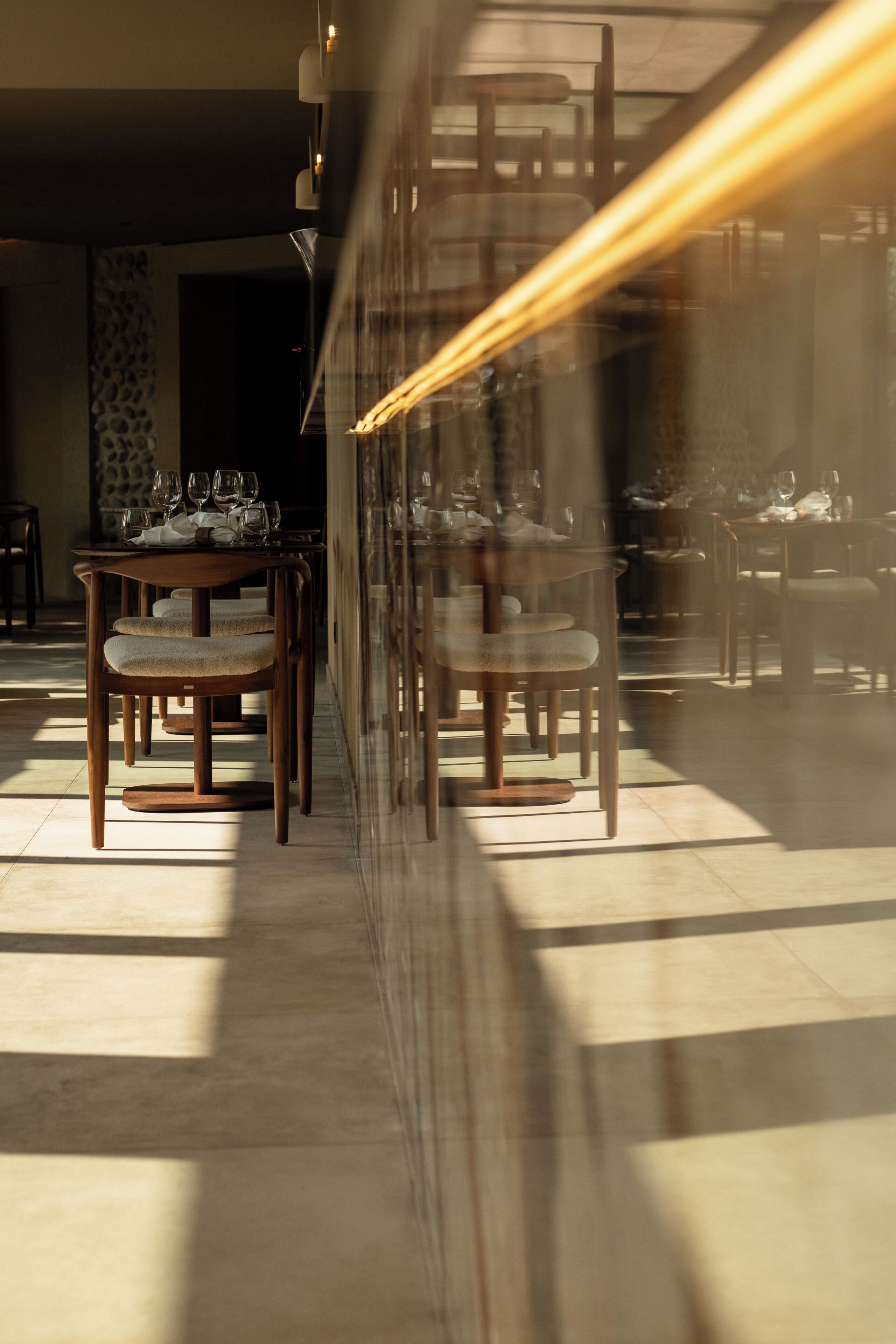 Un comedor con mesas y sillas, luz solar entrando por una ventana y vistas a la calle.