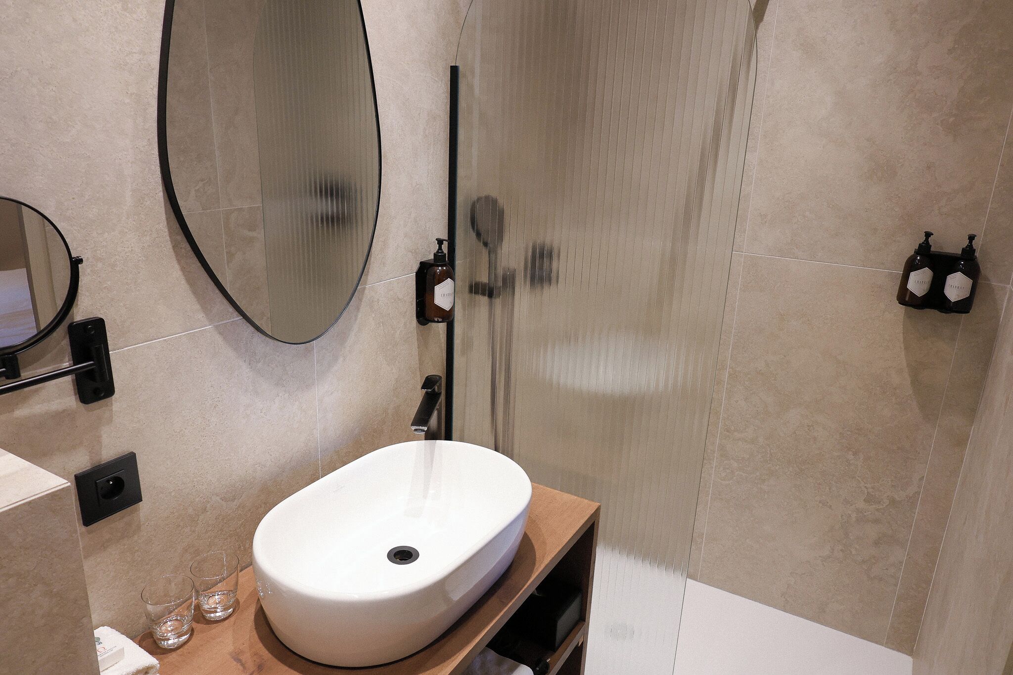 A bathroom with a white sink, a mirror, a handheld showerhead, and two bottles of shampoo on the wall.
