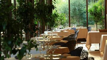 A restaurant with tables set for dining, surrounded by large windows and greenery.