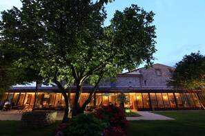 A stone building with a covered outdoor seating area and a tree in the foreground.