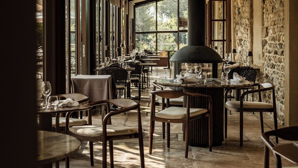 A restaurant with high ceilings, stone walls, and large windows allowing natural light. Tables and chairs are arranged for dining. - La Maison Chabran - Hôtel Restaurants (Pont-de-l'Isere)