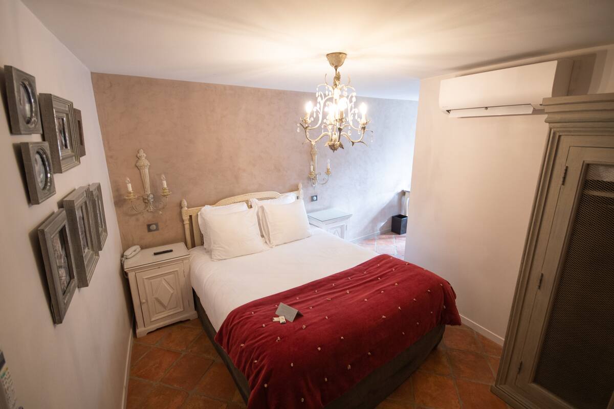 A bedroom with a bed, nightstand, wall-mounted lamp, and a window.