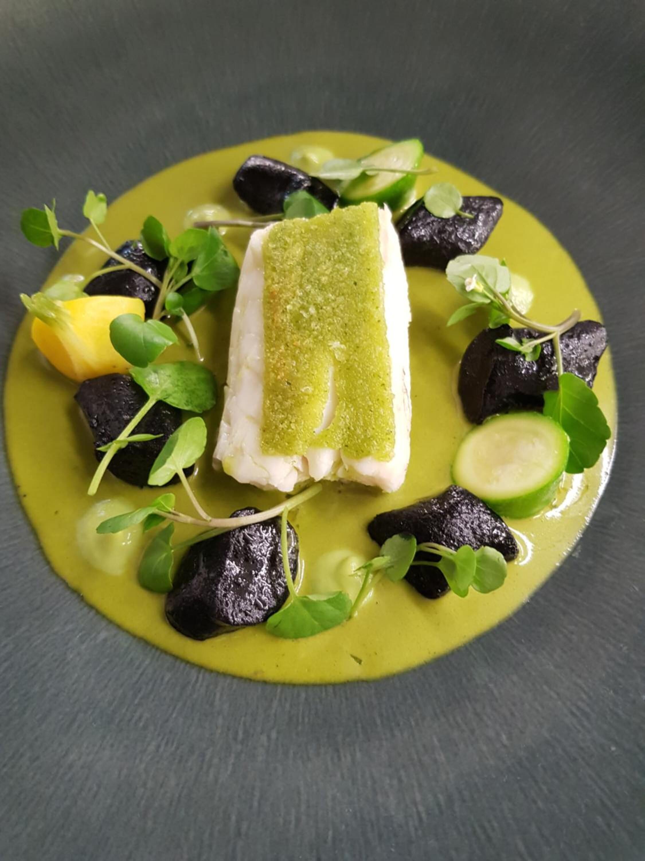 Un plato con pescado, aceitunas negras y verduras verdes.