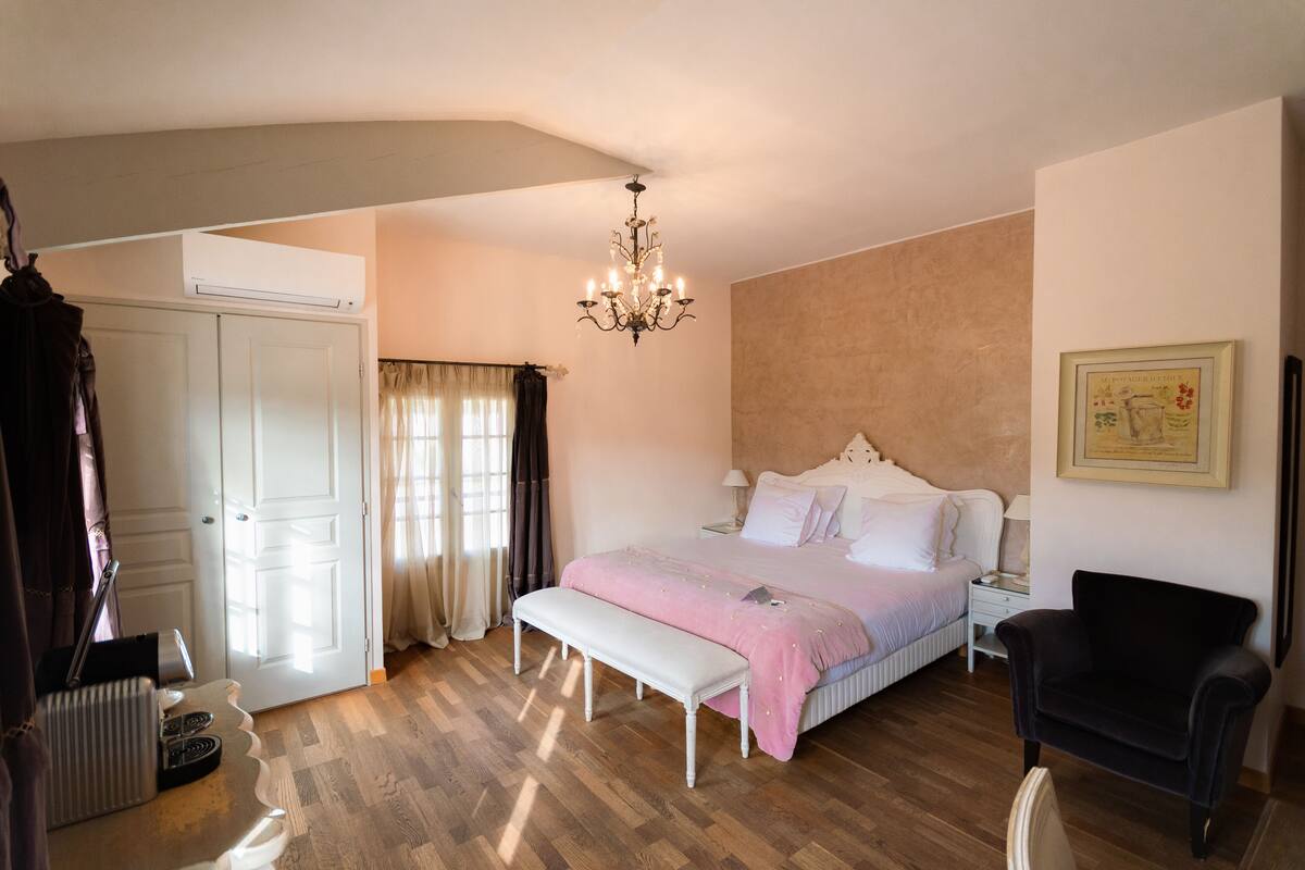 A bedroom with a bed, a bench, a chair, a desk, and an air conditioning unit.