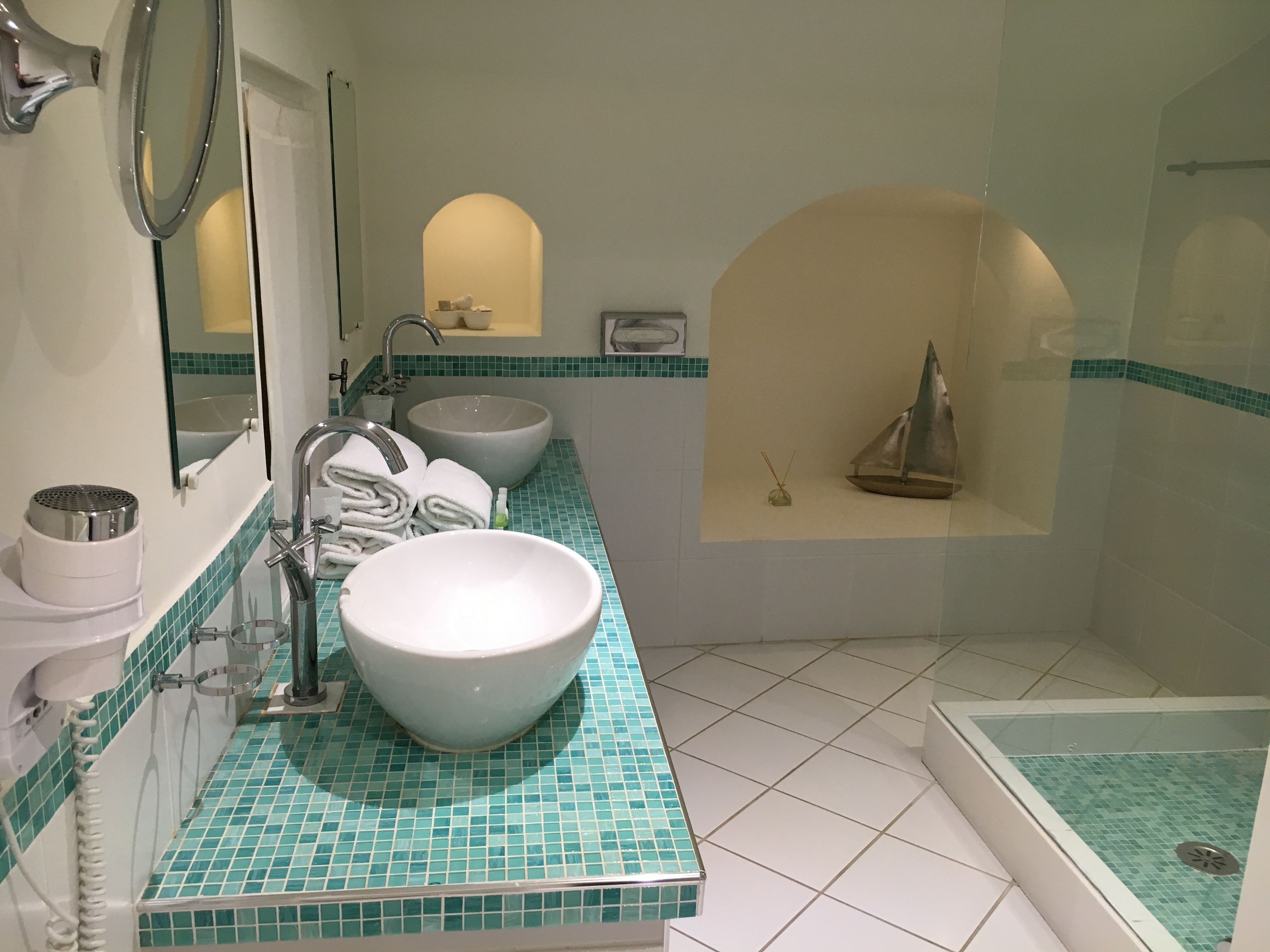A bathroom with a large white sink, a mirror, a towel rack, a small shelf with toiletries, and a bathtub with a tiled floor.