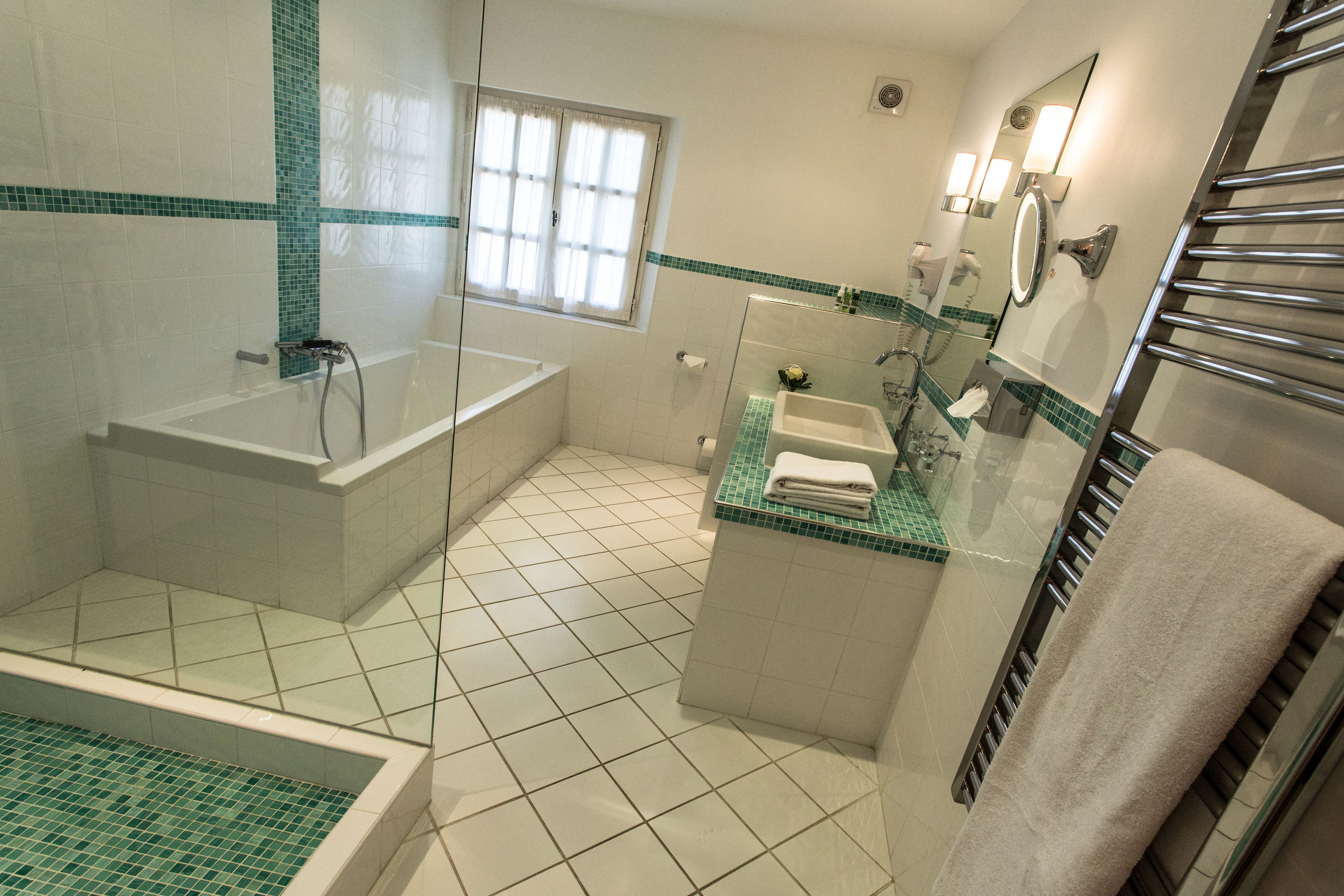 Une salle de bain équipée d’une baignoire, d’une douche, d’un lavabo et d’un espace douche séparé par des parois en verre.