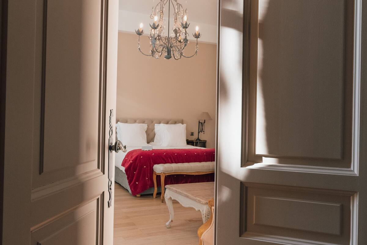 A room with a bed, a chandelier, and a wooden bench.