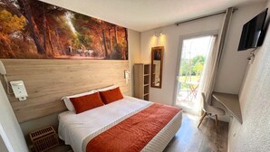 Un dormitorio con una cama grande, un cuadro en la pared, un televisor y un ventanal corredera al exterior.