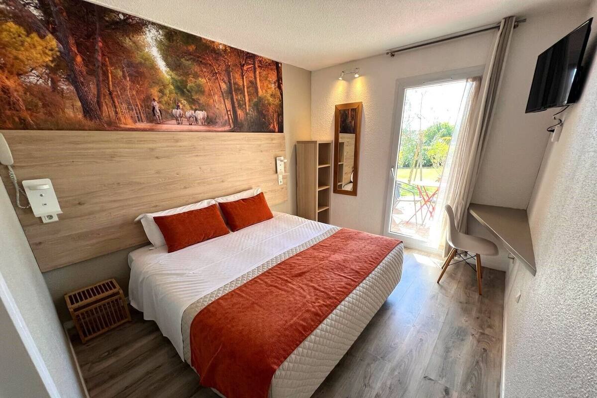 A bedroom with a large bed, a painting on the wall, a TV, and a sliding glass door to the outside.