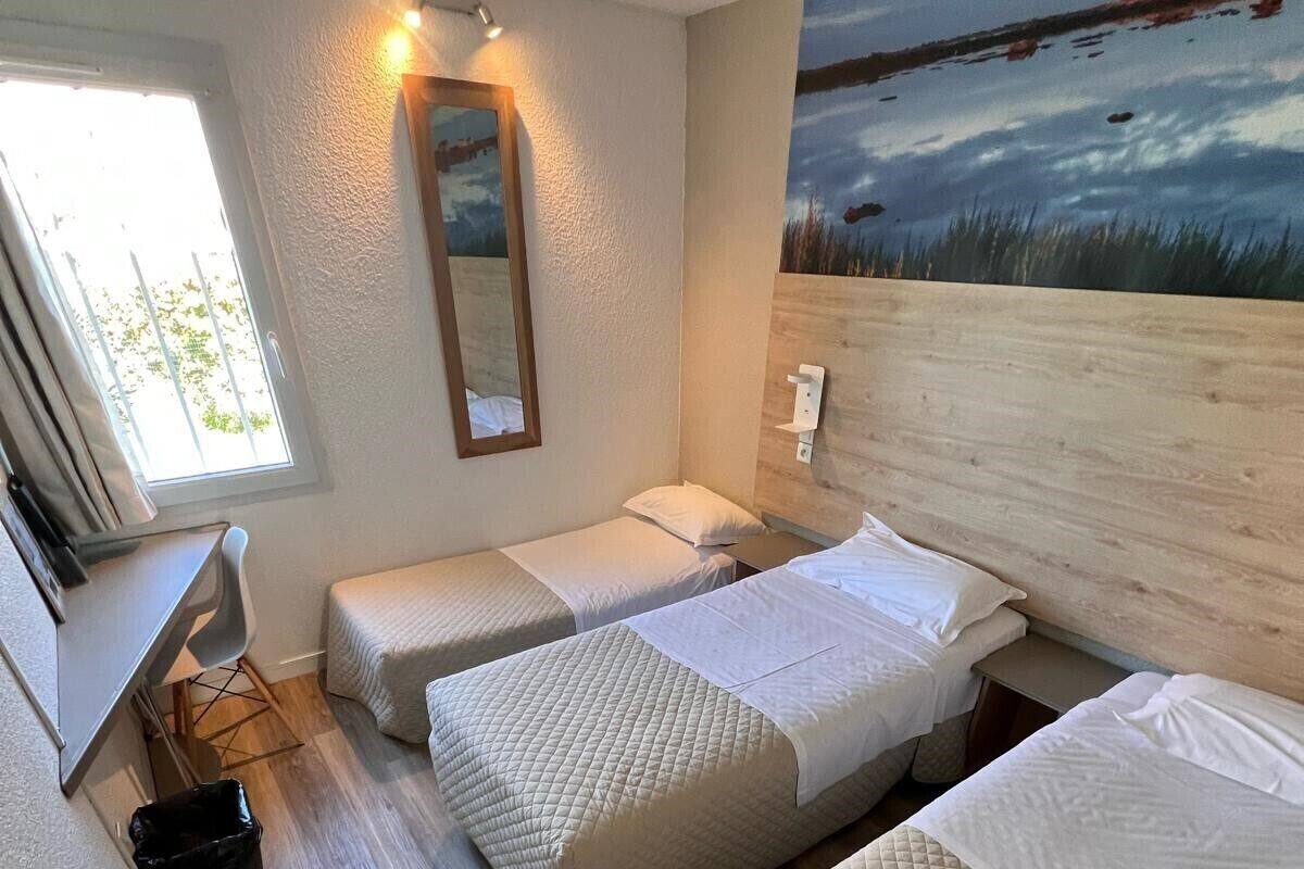 A room with three beds, a desk, a chair, and a painting on the wall.