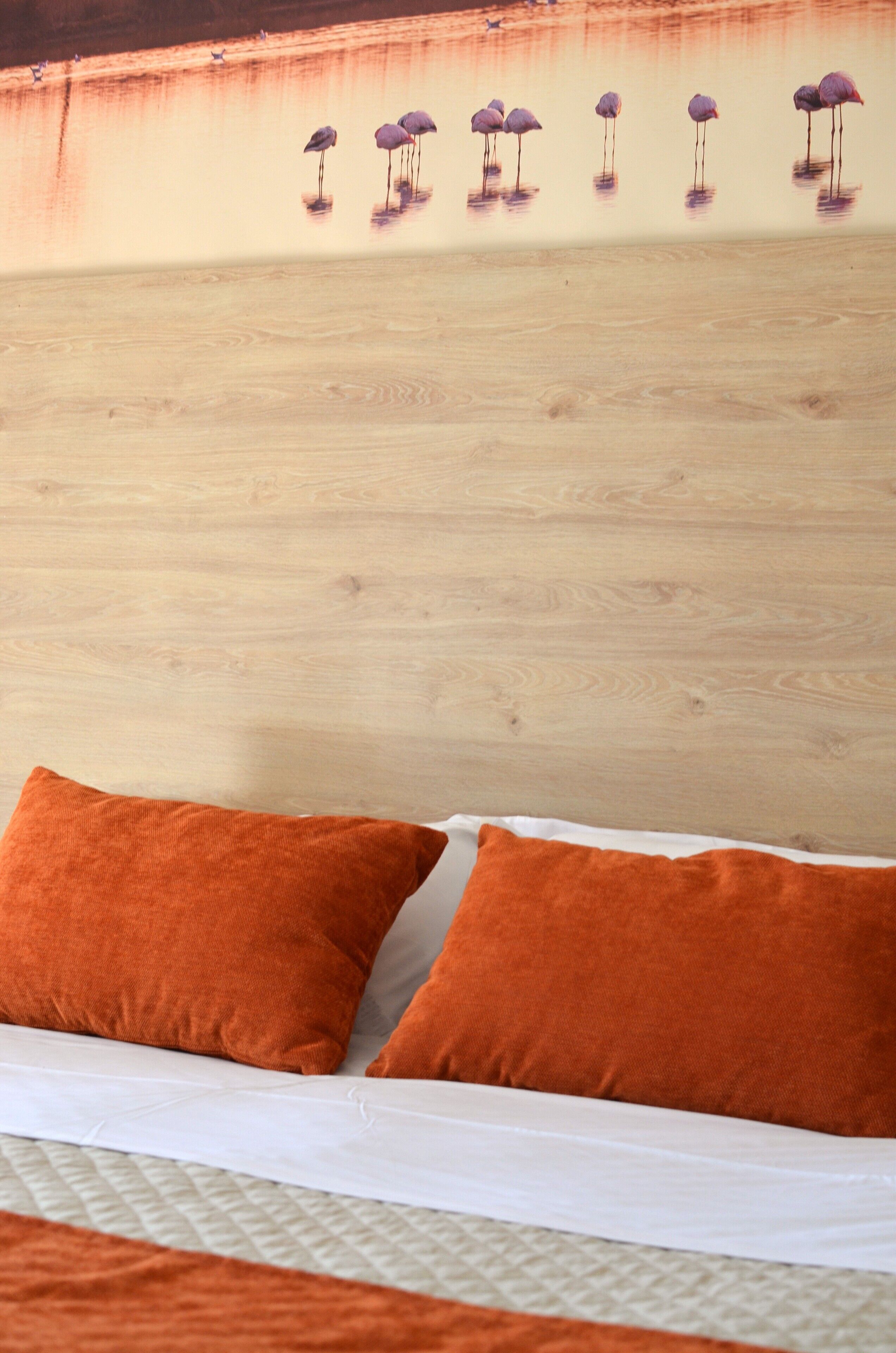 A bed with two orange pillows and a wooden headboard with a wall mural of flamingos.