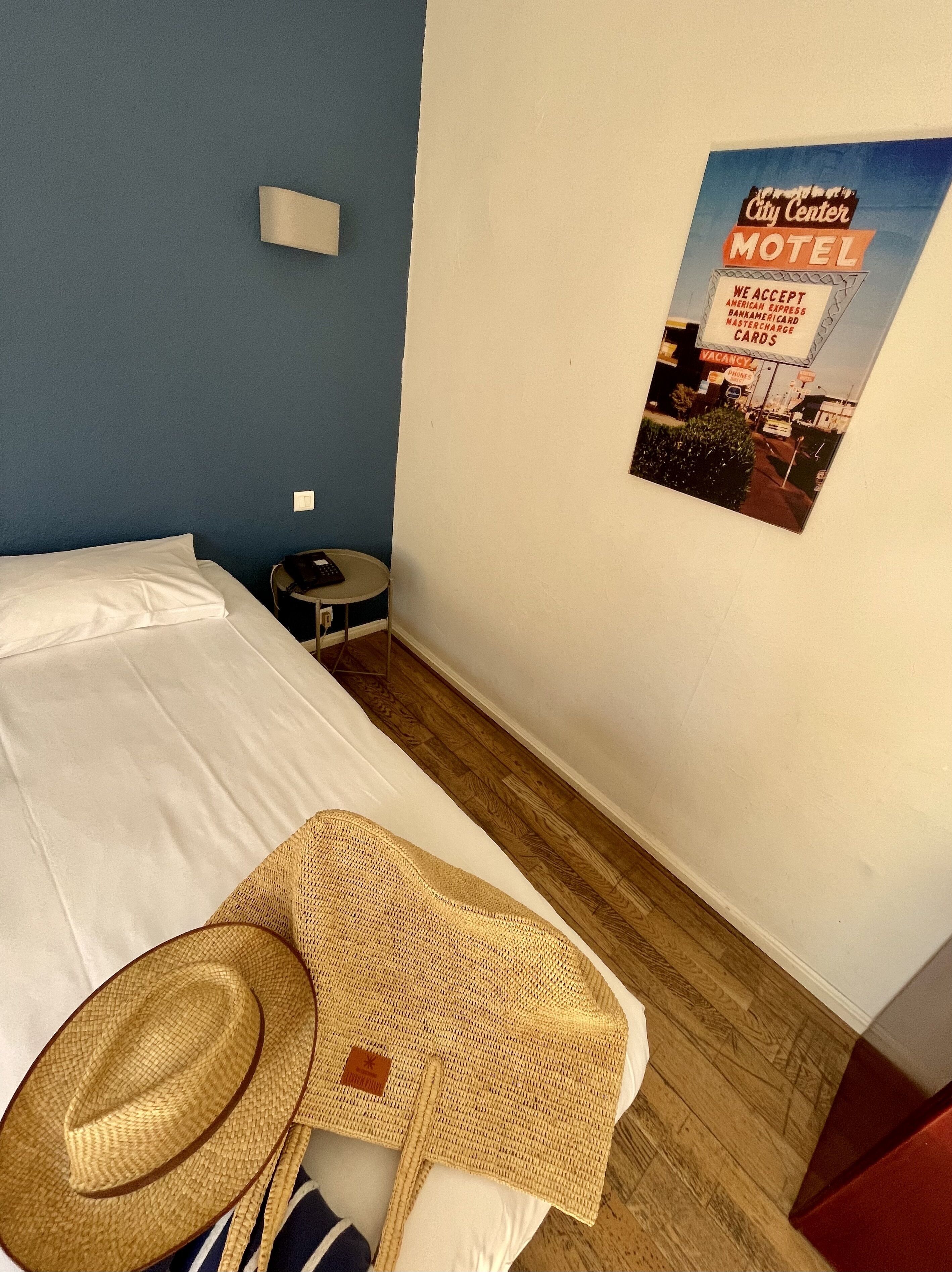 A hotel room with a bed, a small round table, a wall-mounted light, and a poster advertising a City Center Motel.