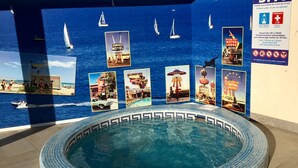 Un espace piscine bordé de carreaux, entouré d’un mur bleu orné d’affiches sur le thème de la marine.