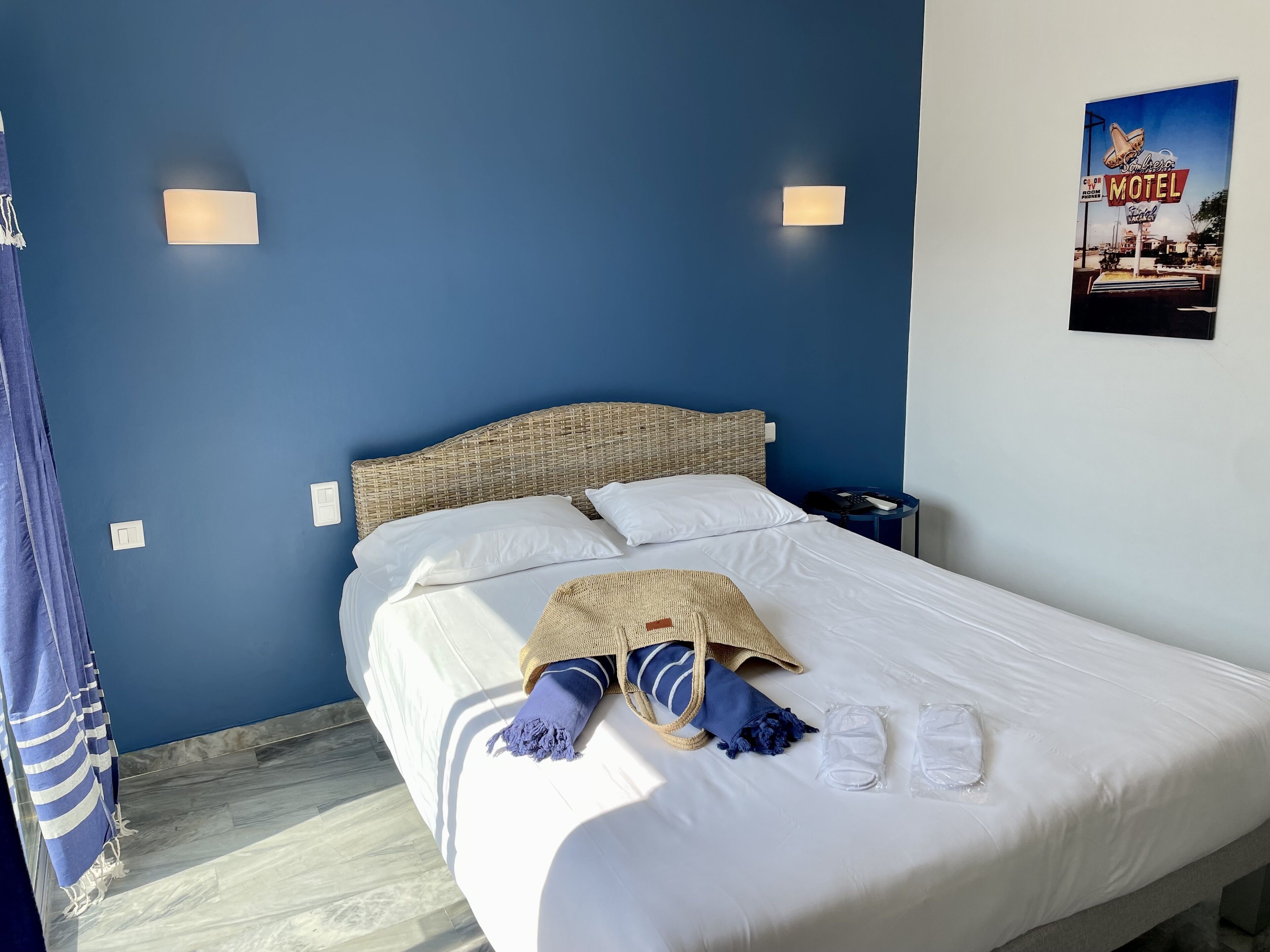 Ein ordentlich bezogenes Bett mit weißen Leinen, einem gewebten Kopfteil und einem blau-weiß gestreiften Handtuch.