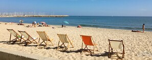 A beach with rows of beach chairs and umbrellas, a rocky breakwater in the background, and calm sea. - Cit’Hôtel Amérique (Palavas-les-Flots)