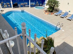 Une piscine dotée d’une terrasse carrelée, de chaises longues et d’un mur décoratif orné de photos.