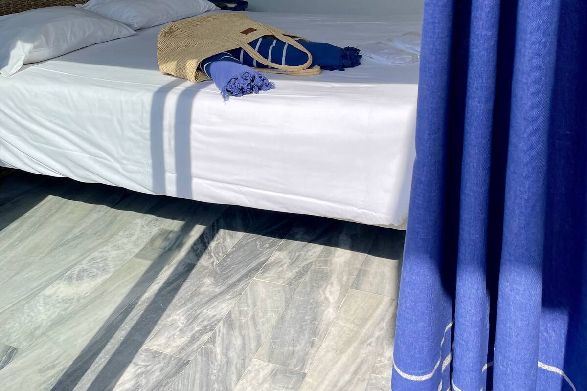 Ein Bett mit weißen Leinen, einer gewebten Tasche und einer blauen Decke.