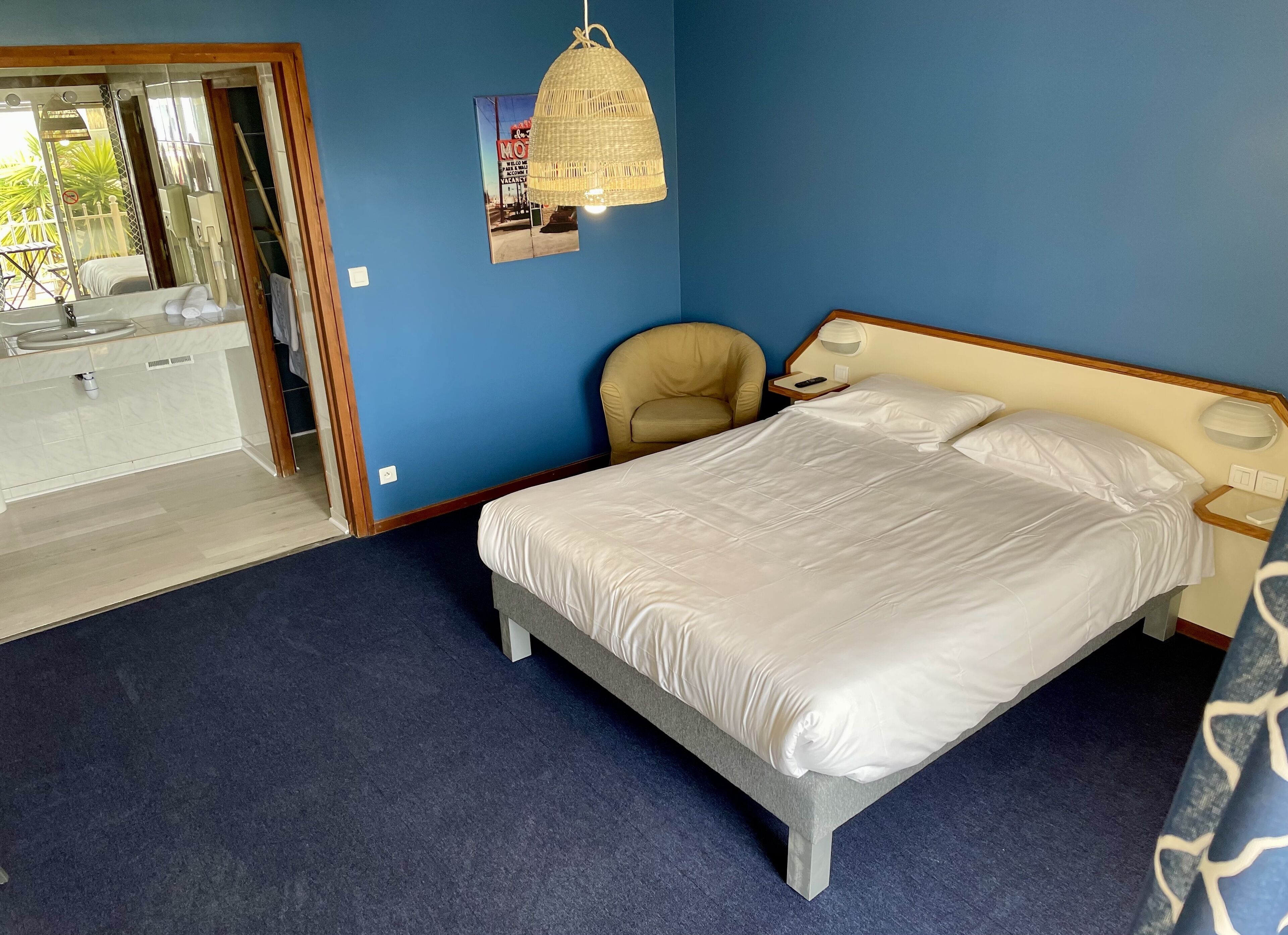 A bedroom with a bed, a chair, a nightstand, and a hanging light fixture.