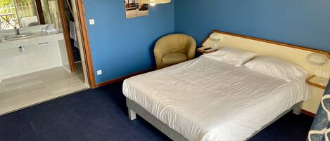 A bedroom with a bed, a chair, a nightstand, and a hanging light fixture.