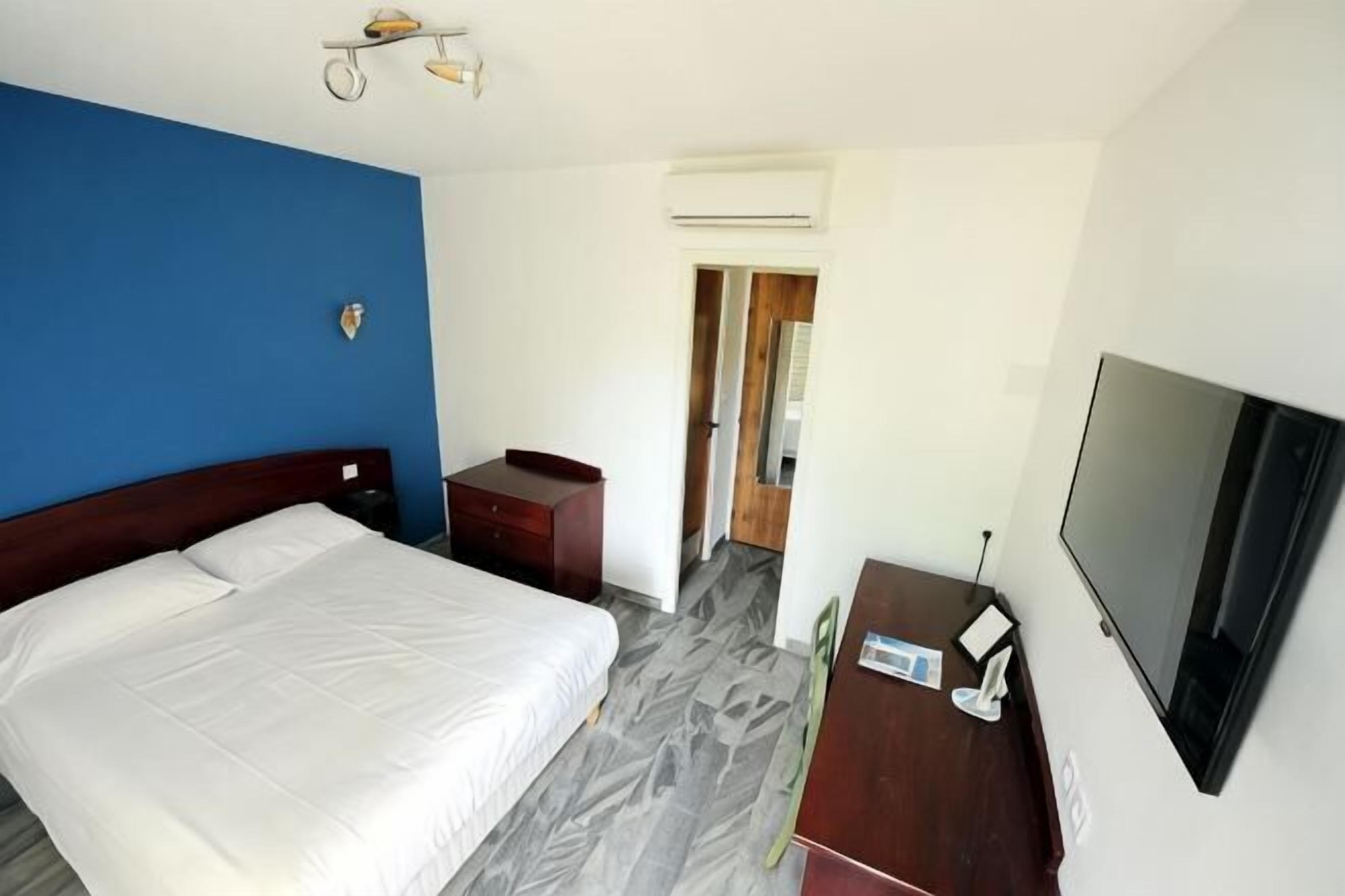Hotellihuone, jossa on sänky, työpöytä, tuoli, televisio ja ilmastointilaite.
