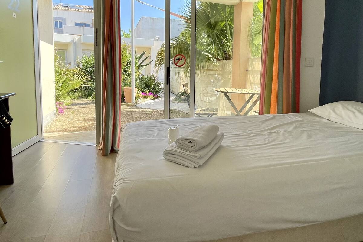 Ein Hotelzimmer mit Bett, Blick nach draußen und einem Balkon mit Tisch und Stühlen.