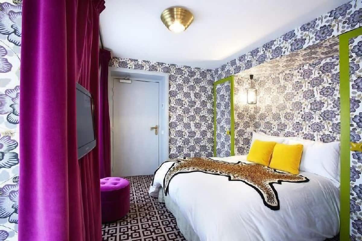 A bedroom with a patterned wallpaper, a bed with a leopard print blanket, and a television.