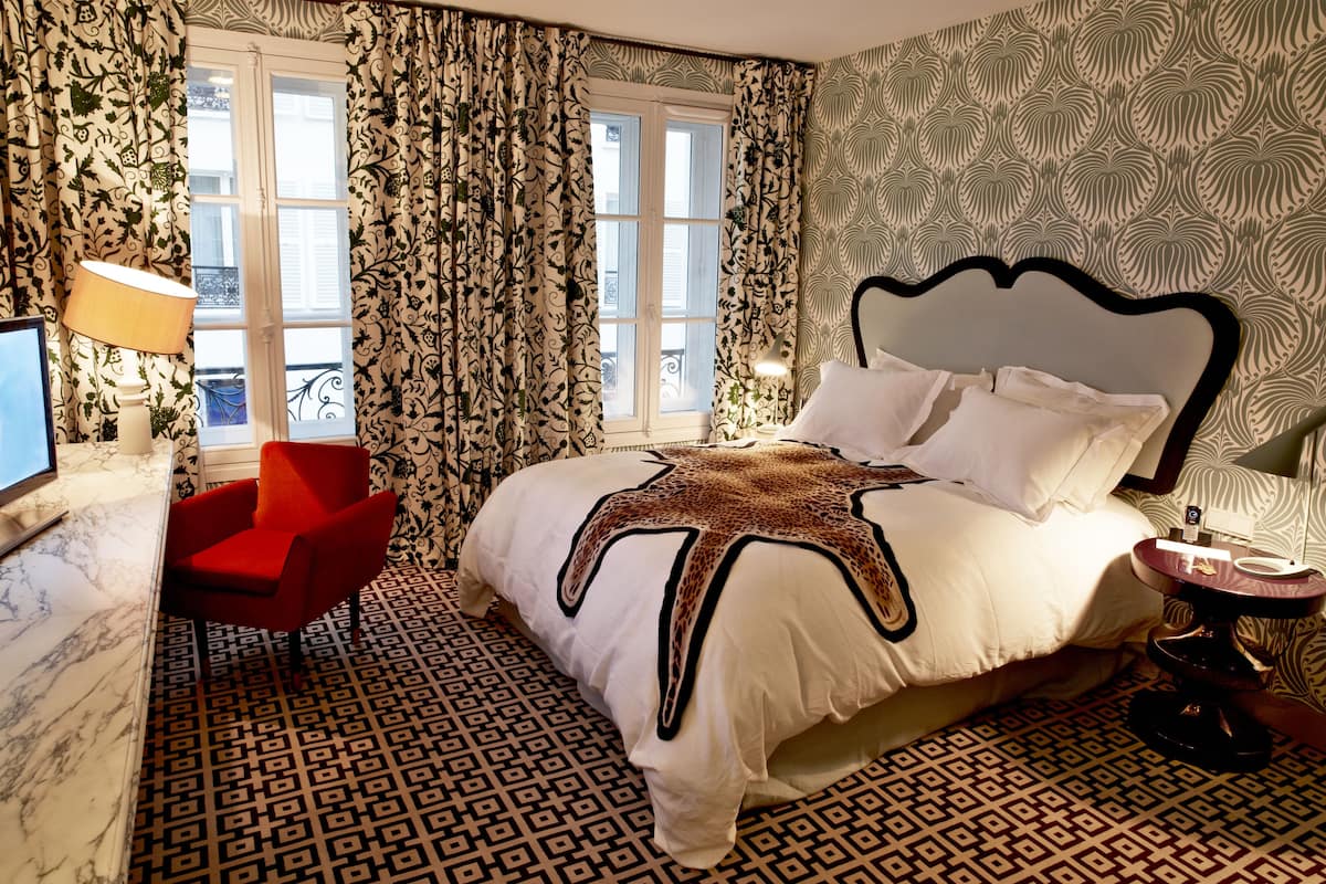 A hotel room with a bed, a red chair, a TV, and patterned curtains.