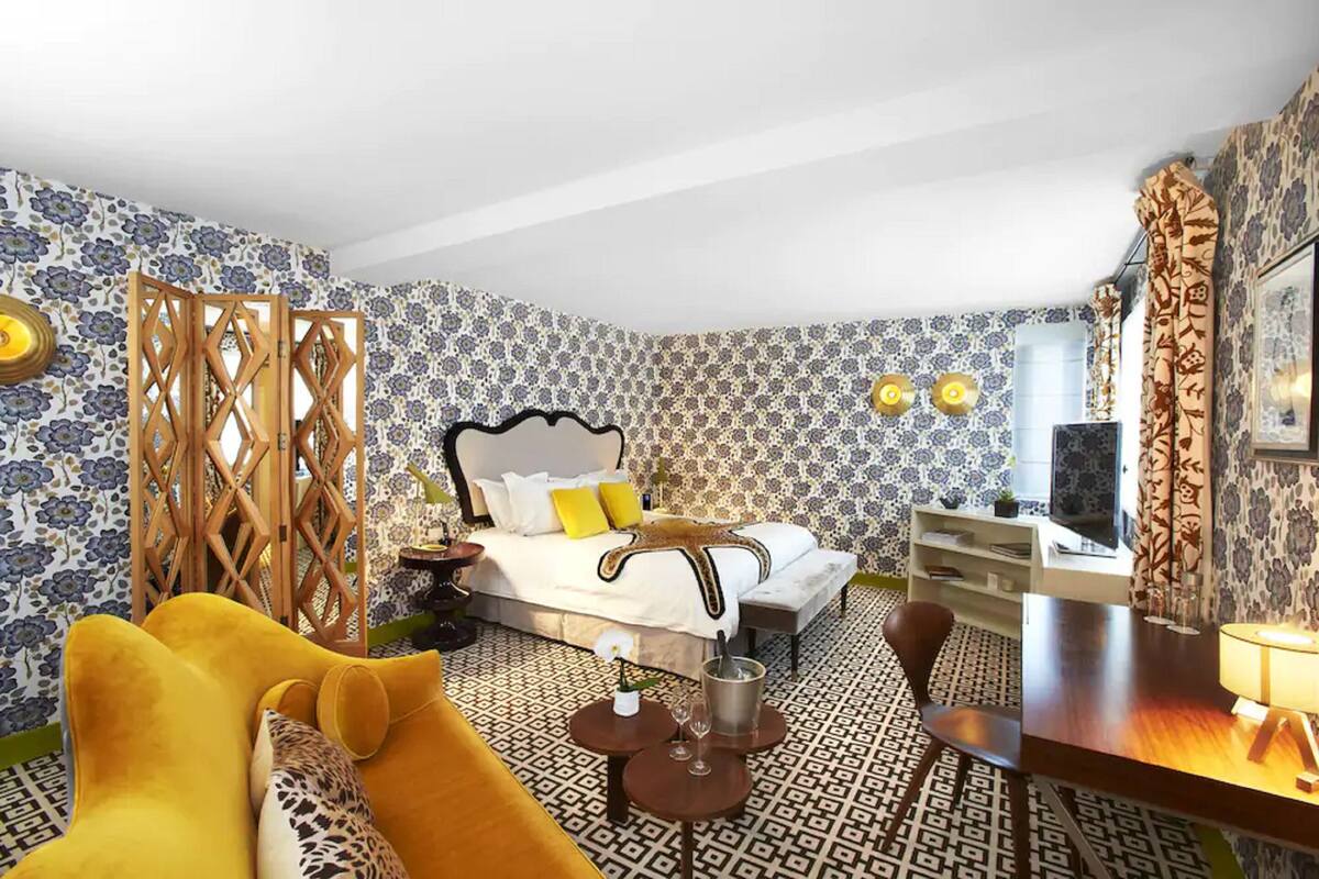 A hotel room with a bed, a desk, a chair, a small table with a lamp, and a decorative screen.