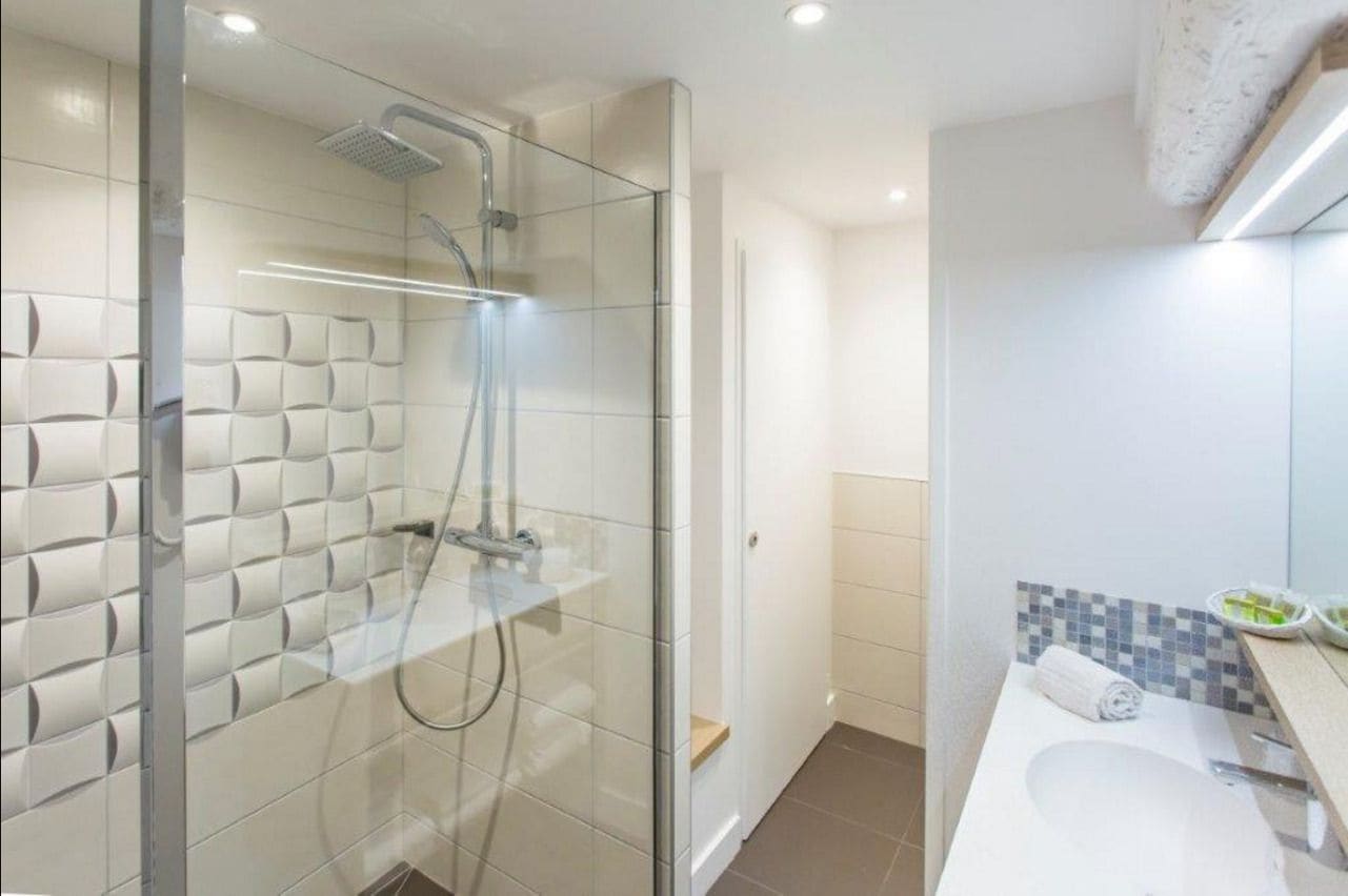 Une salle de bain moderne avec une douche à parois de verre, un lavabo blanc et un mur recouvert de carreaux.