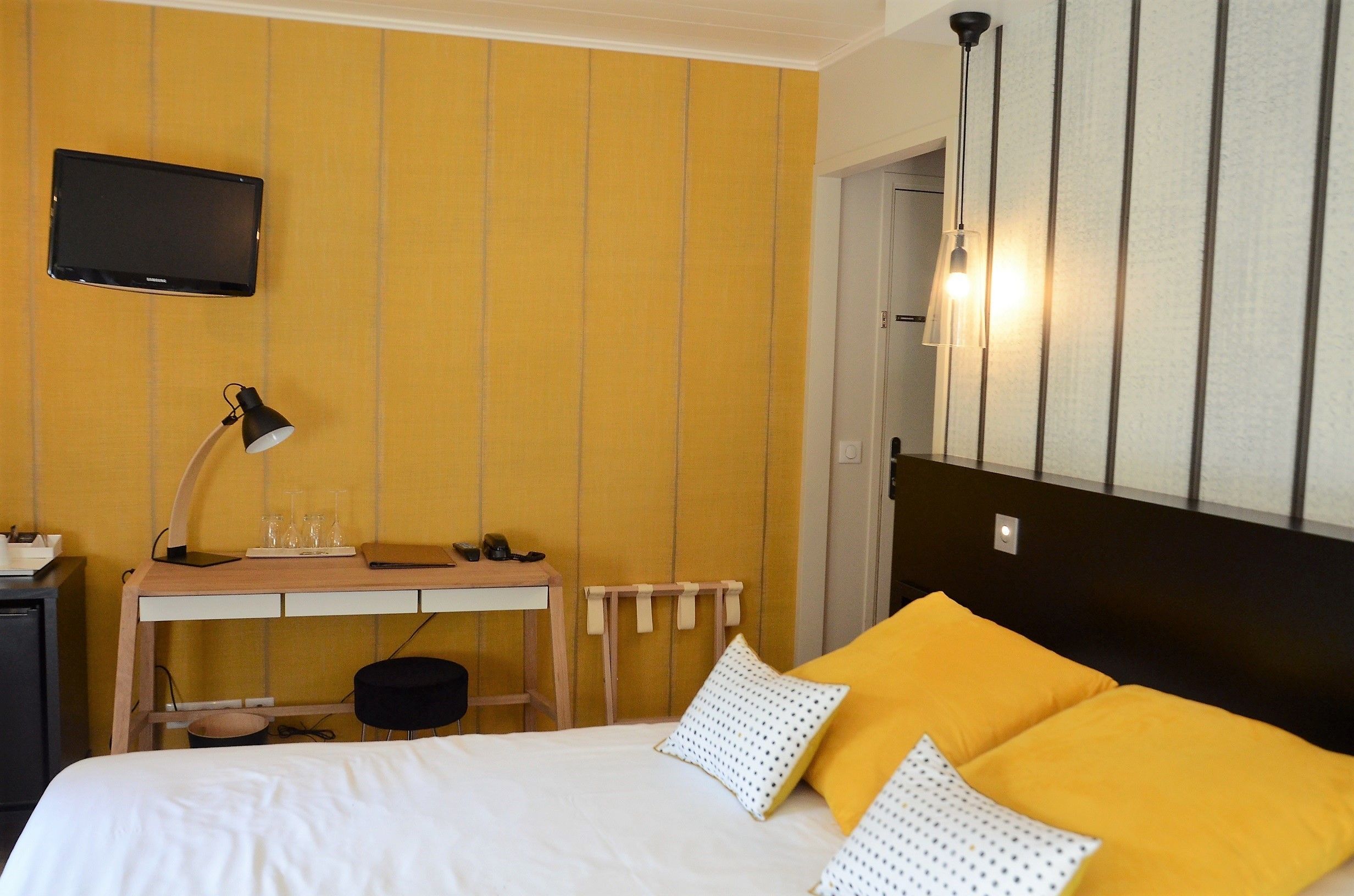 Une chambre d’hôtel avec un lit, un bureau doté d’une lampe, une télévision et un luminaire fixé au mur.