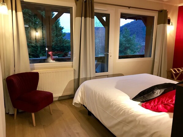 Un dormitorio con una cama, una silla roja y dos ventanas con cortinas.
