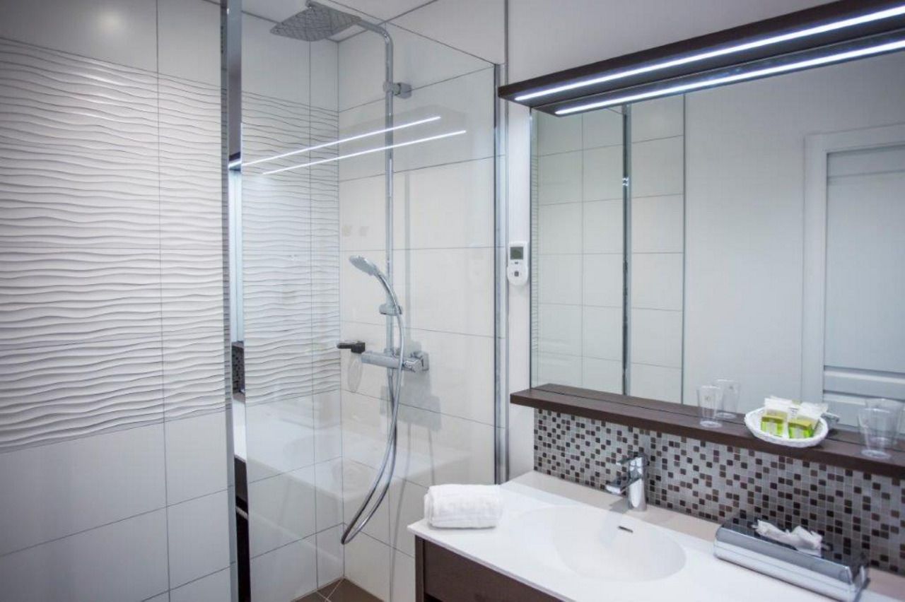 Un baño moderno con cabina de ducha de vidrio, un lavamanos blanco y un espejo con encimera marrón.