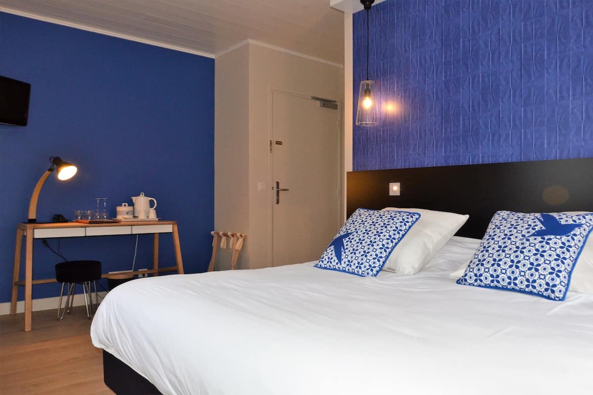 Ein Hotelzimmer mit Bett, Schreibtisch, Stuhl, Lampe und Tür.